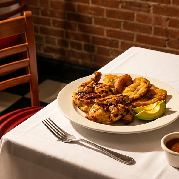Grilled chicken, plantains, and avocado slices on a white plate with two sauces on a table.