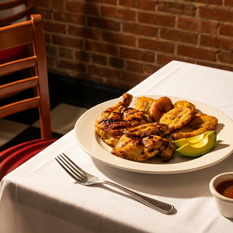 Grilled chicken, plantains, and avocado slices on a white plate with two sauces on a table.